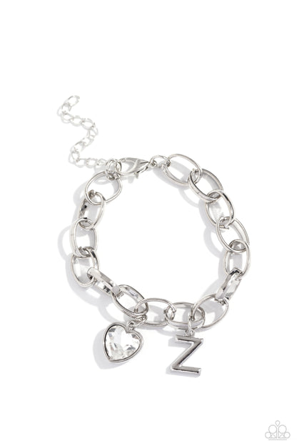 Guess Now Its INITIAL White "Z" Bracelet - Paparazzi Accessories  A simple collection of silver charms — including a white rhinestone heart pressed in a silver frame and a sleek letter "Z" — dance from a chunky silver chain around the wrist, creating a sentimental fringe. Features an adjustable clasp closure.  Sold as one individual bracelet.  New Kit Sku:  P9BA-WTXX-060XX