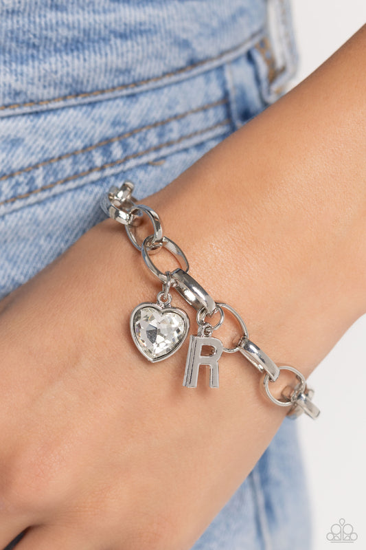Guess Now Its INITIAL White "R" Bracelet - Paparazzi Accessories  A simple collection of silver charms — including a white rhinestone heart pressed in a silver frame and a sleek letter "R" — dance from a chunky silver chain around the wrist, creating a sentimental fringe. Features an adjustable clasp closure.  Sold as one individual bracelet.  New Kit Sku:  P9BA-WTXX-052XX