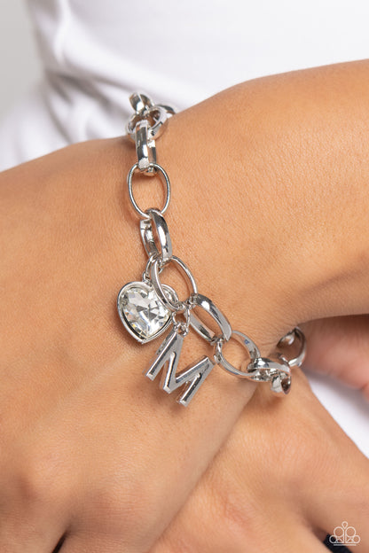Guess Now Its INITIAL White "M" Bracelet - Paparazzi Accessories  A simple collection of silver charms — including a white rhinestone heart pressed in a silver frame and a sleek letter "M" — dance from a chunky silver chain around the wrist, creating a sentimental fringe. Features an adjustable clasp closure.  Sold as one individual bracelet.  New Kit Sku:  P9BA-WTXX-047XX