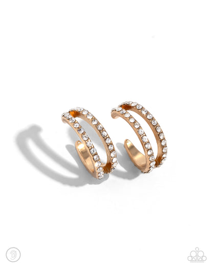 Monochromatic Mystique Gold Ear Cuff - Paparazzi Accessories  Dusted in dainty white rhinestones, two thin gold bars crisscross around the ear for a dynamic statement. Features a smooth surface for sliding ability to desired position on the ear. Due to its structure, adjusting capability is limited.  Sold as one pair of cuff earrings.  SKU: P5PO-CFGD-280XX