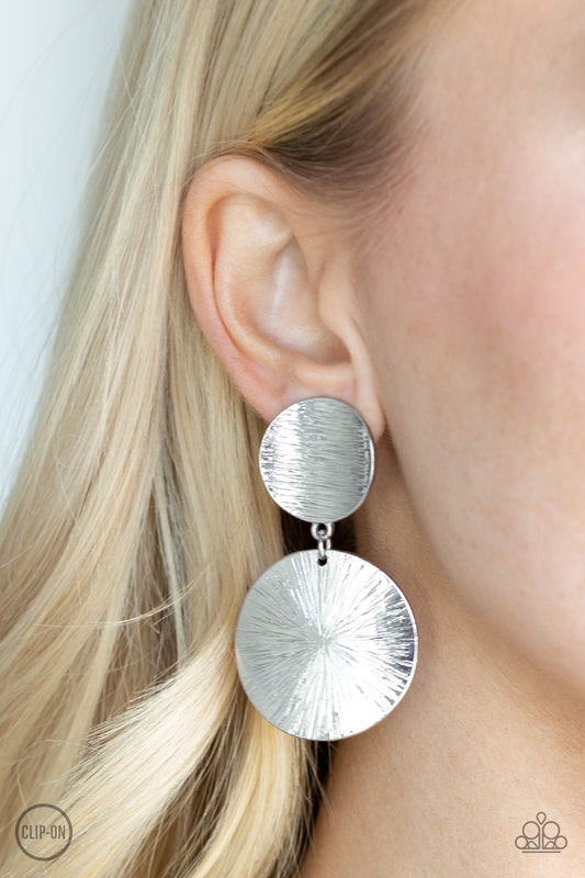 BRIGHT On Cue Silver Clip-On Earring - Paparazzi Accessories Item #E115 Streaked in shimmery linear textures, a beveled silver disc gives way to a larger beveled disc for a refined look. Earring attaches to a standard clip on fitting. All Paparazzi Accessories are lead free and nickel free!  Sold as one pair of clip-on earrings.