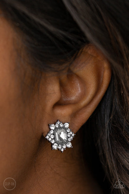 Interstellar Sparkle - Black Item #E324 Featuring sleek gunmetal fittings, dainty white rhinestones coalesce around a glittery white emerald style rhinestone center for a stellar look. Earring attaches to a standard clip-on fitting. All Paparazzi Accessories are lead free and nickel free!  Sold as one pair of clip-on earrings.